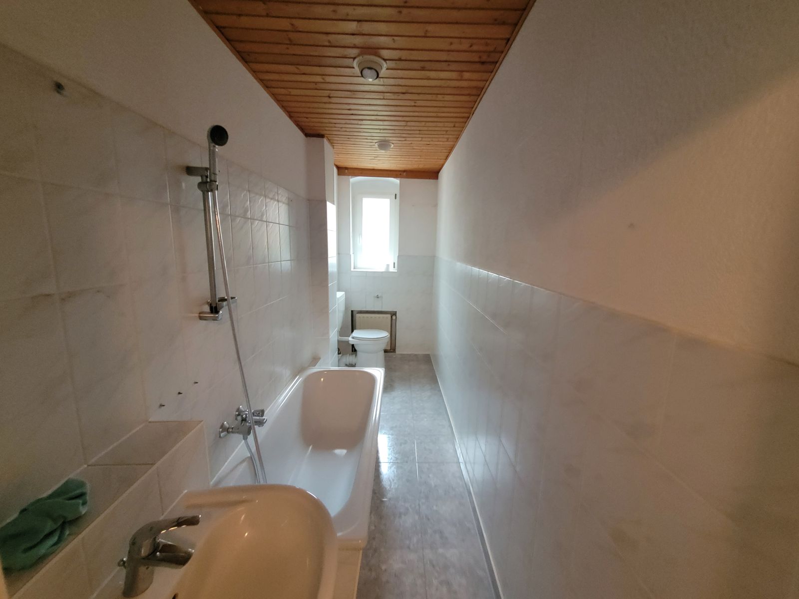 Bad im Berliner Altbau vor der Sanierung: schmaler Schlauch mit Wanne, WC und Holzdecke aus den Achtzigern