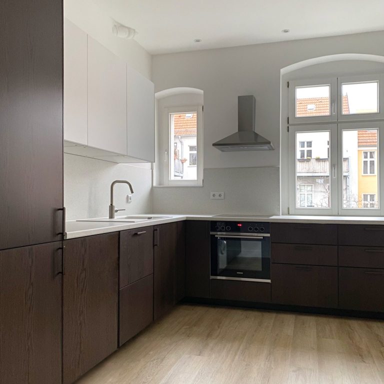 Küche einer Berliner Altbauwohnung Moderne Küche mit Holz- und weißen Schränken, Fenstern und Edelstahlabzugshaube.